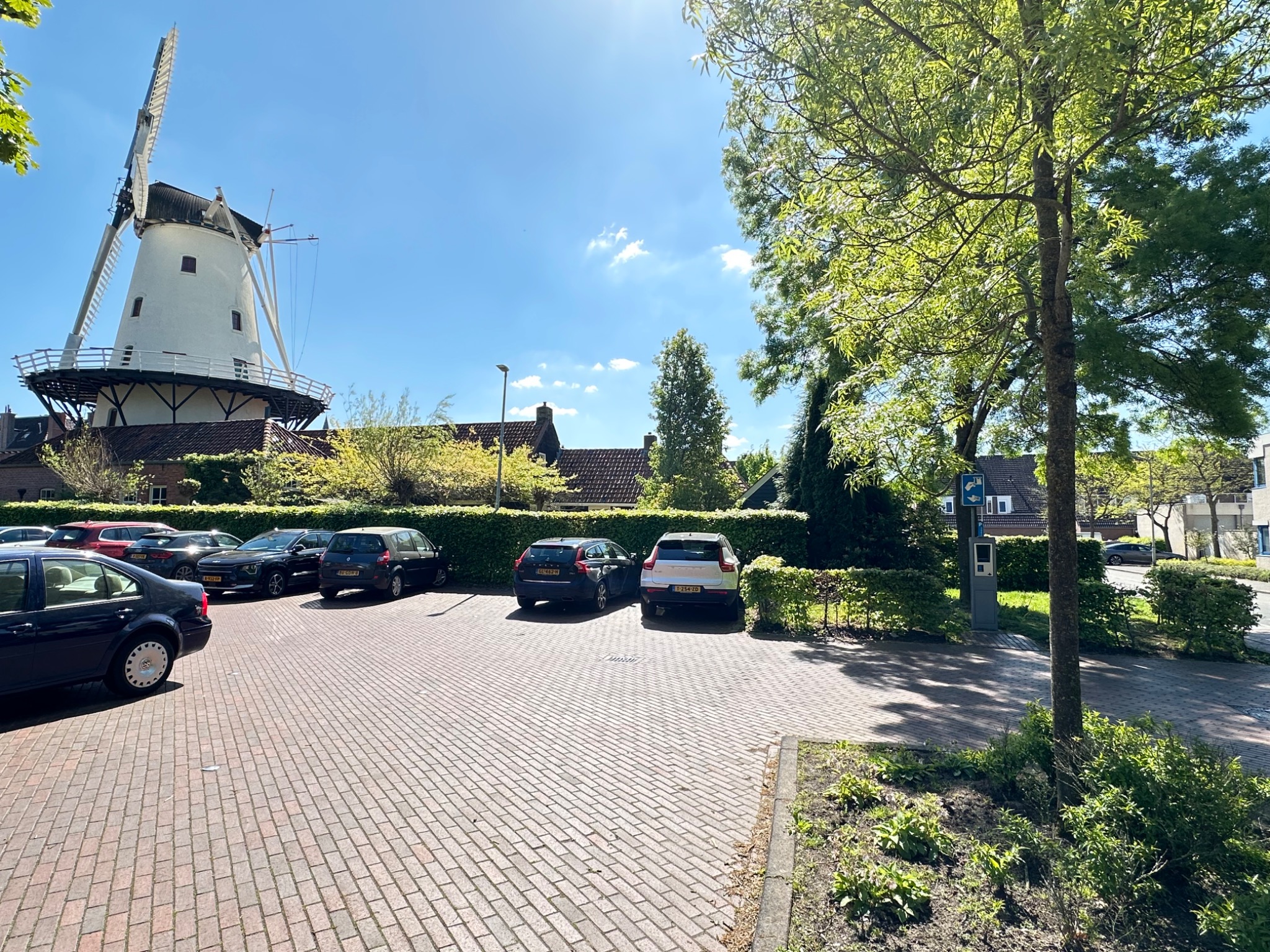 Molen De Hoop met de omliggende gebouwen, bomen en het parkeerterrein op de voorgrond.