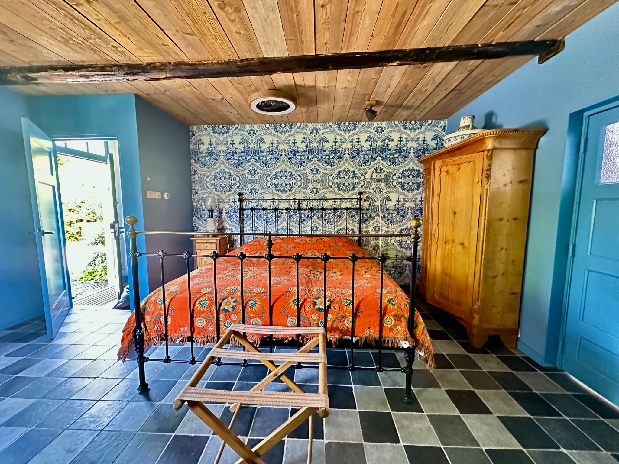 Het bed met oranje bedsprei, blauwe wanden en houten balken in Het Swarte Schoap.